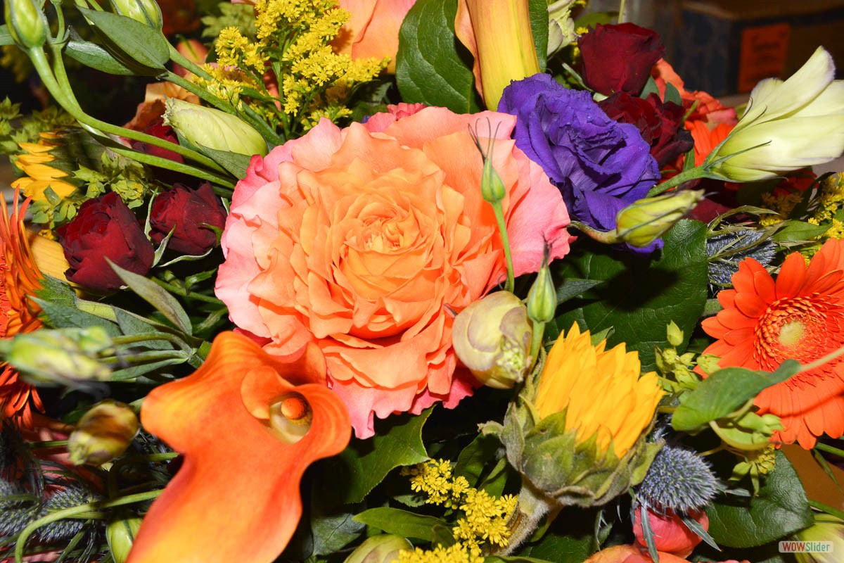 A very colorful bouquet of flowers featuring an orange centerpiece accented by red roses and more!