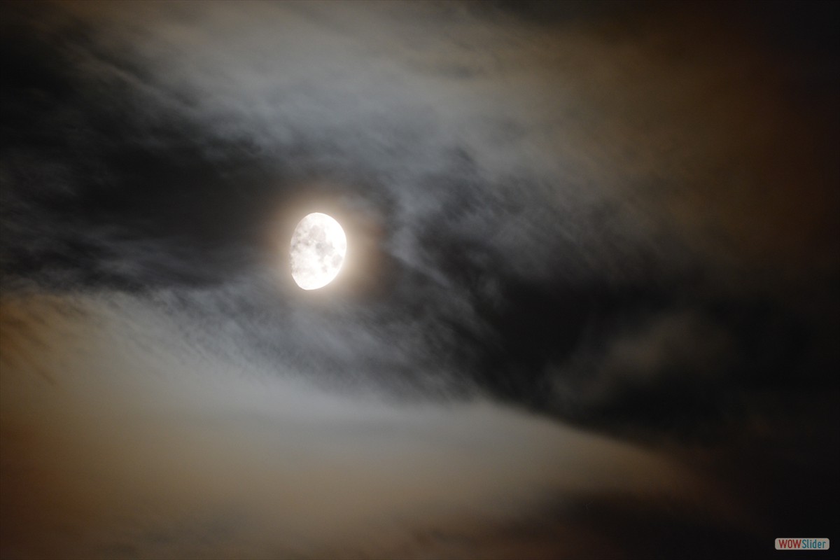 A fine harvest moon surrounded by whistful clouds shines brightly.